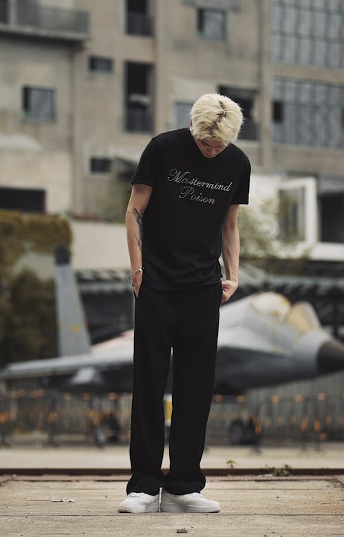 Photo of a Young Man Standing on a Pavement, and Small Airplane in Background