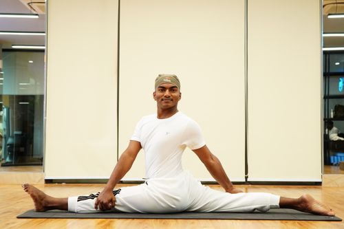 Free Athletic man in white sportswear doing splits on a mat in a gym setting, demonstrating flexibility. Stock Photo
