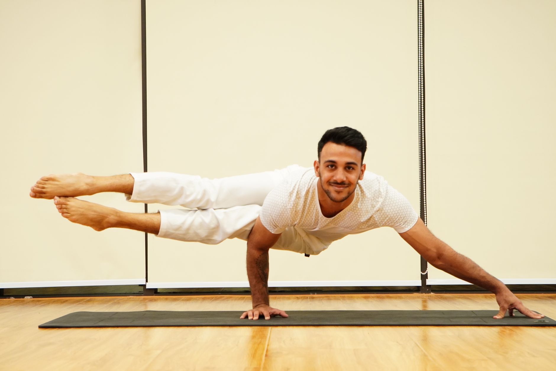 A man balances in an advanced yoga pose on a mat indoors, showcasing strength and focus.