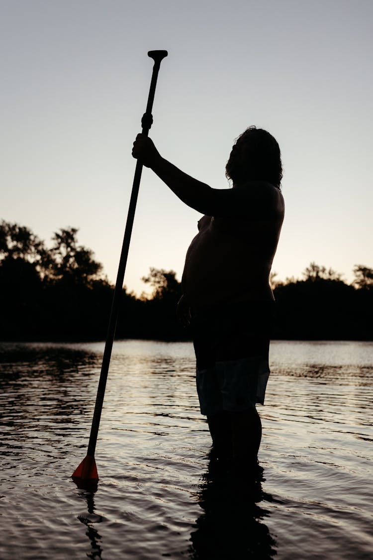 Silhouette Of A Man Standing In The Water And Holding A Paddle 