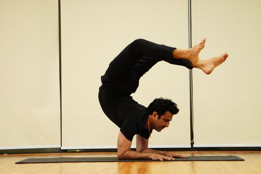 A man demonstrates impressive flexibility and skill performing a handstand on a mat indoors, showcasing balance and athleticism.