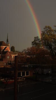A stunning rainbow arcs over a quaint town, with charming brick buildings and lush trees.