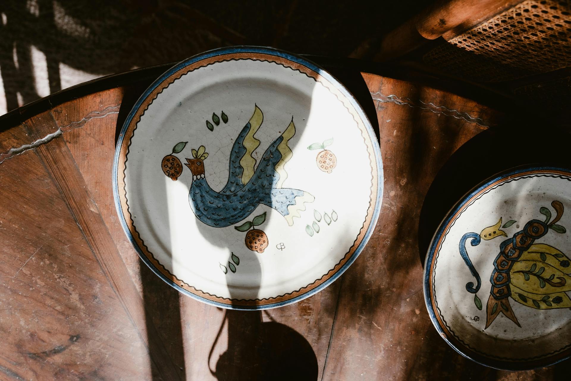 Vintage hand-painted ceramic plates with bird motifs on a wooden table in soft natural light.