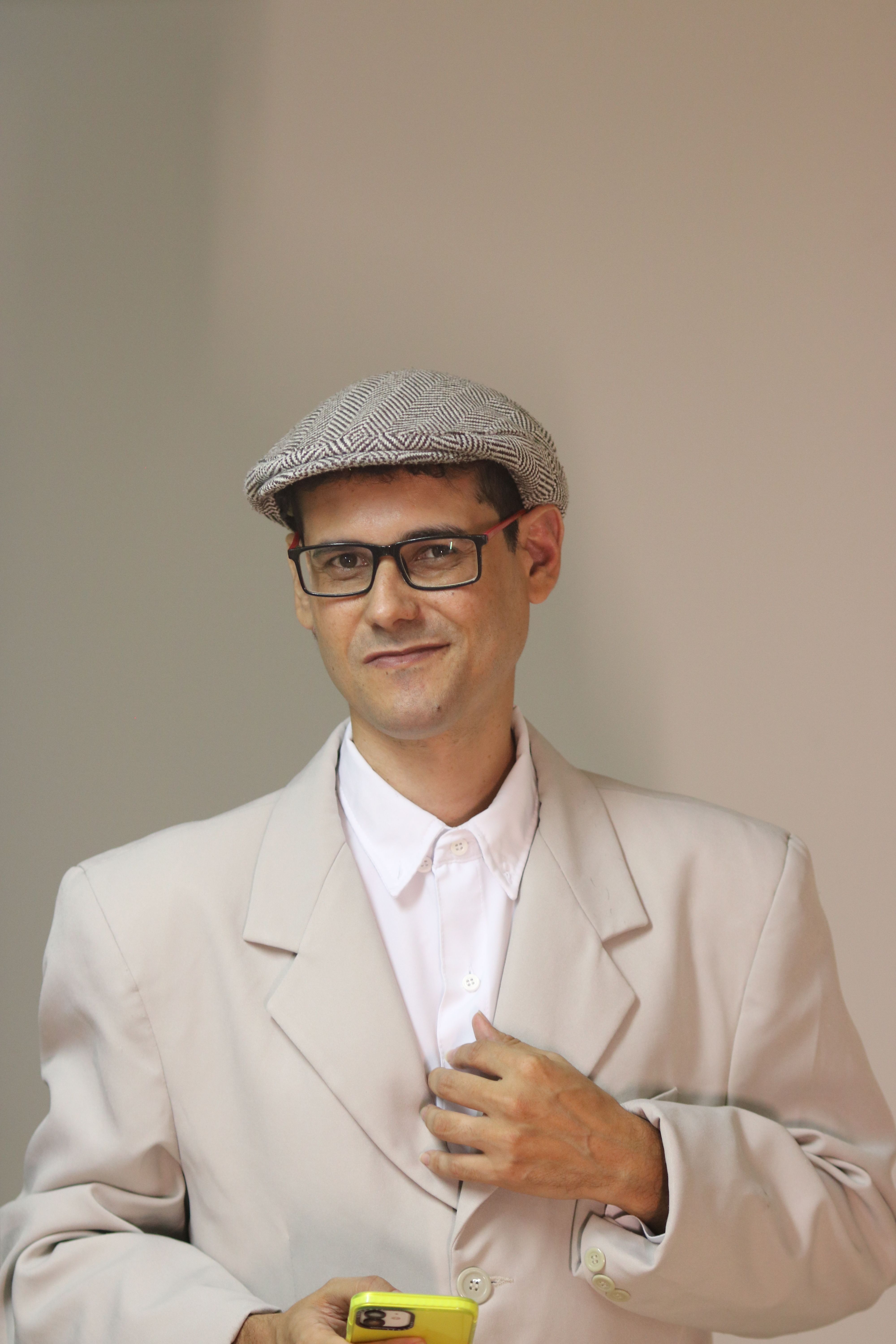 Man in a beige blazer and cap holding a smartphone, exuding elegant style.