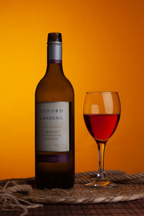 Free Elegant wine bottle and glass on vibrant orange backdrop, perfect for beverage presentations. Stock Photo