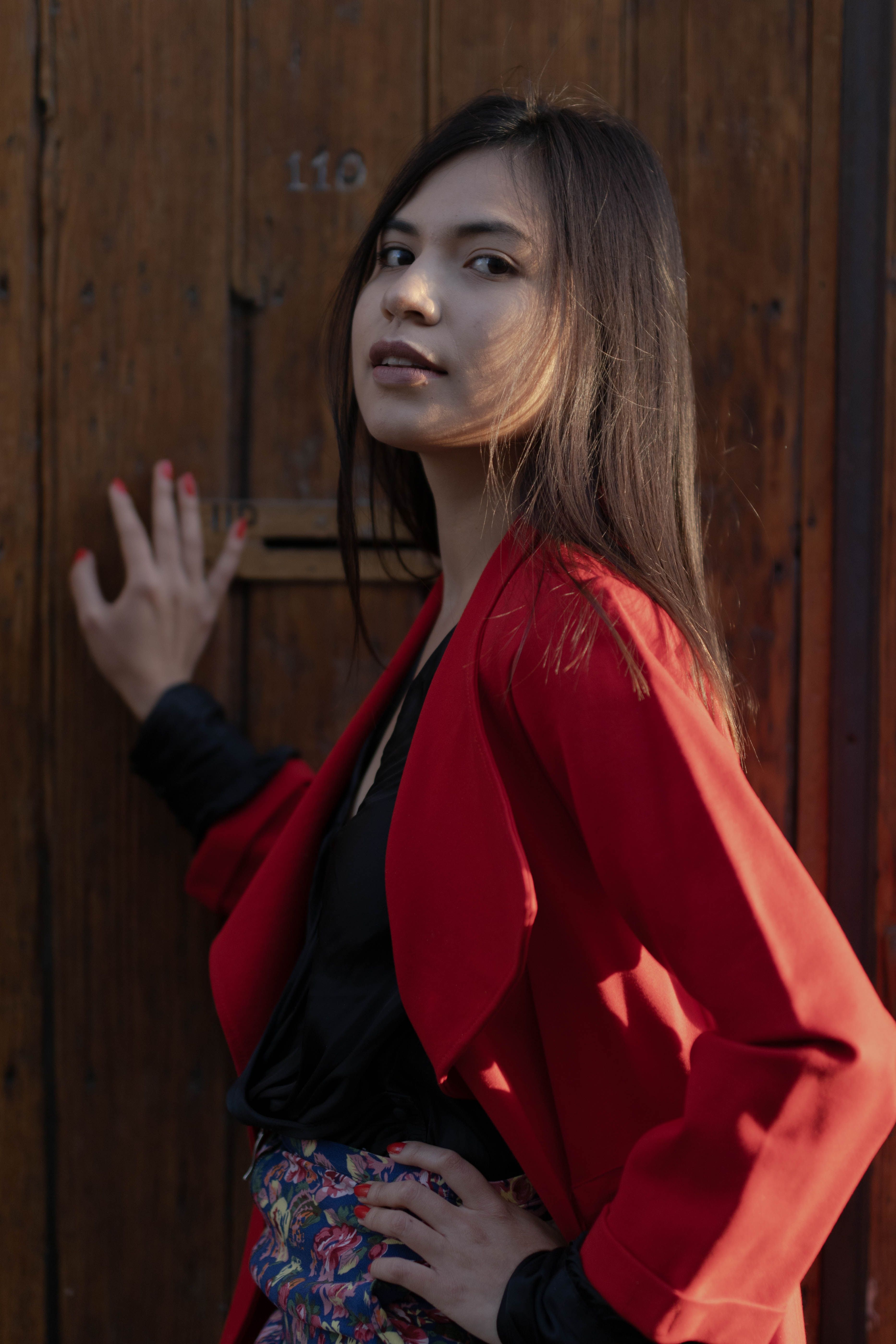 Portrait of a brunette woman in a red blazer posing against a wooden backdrop.
