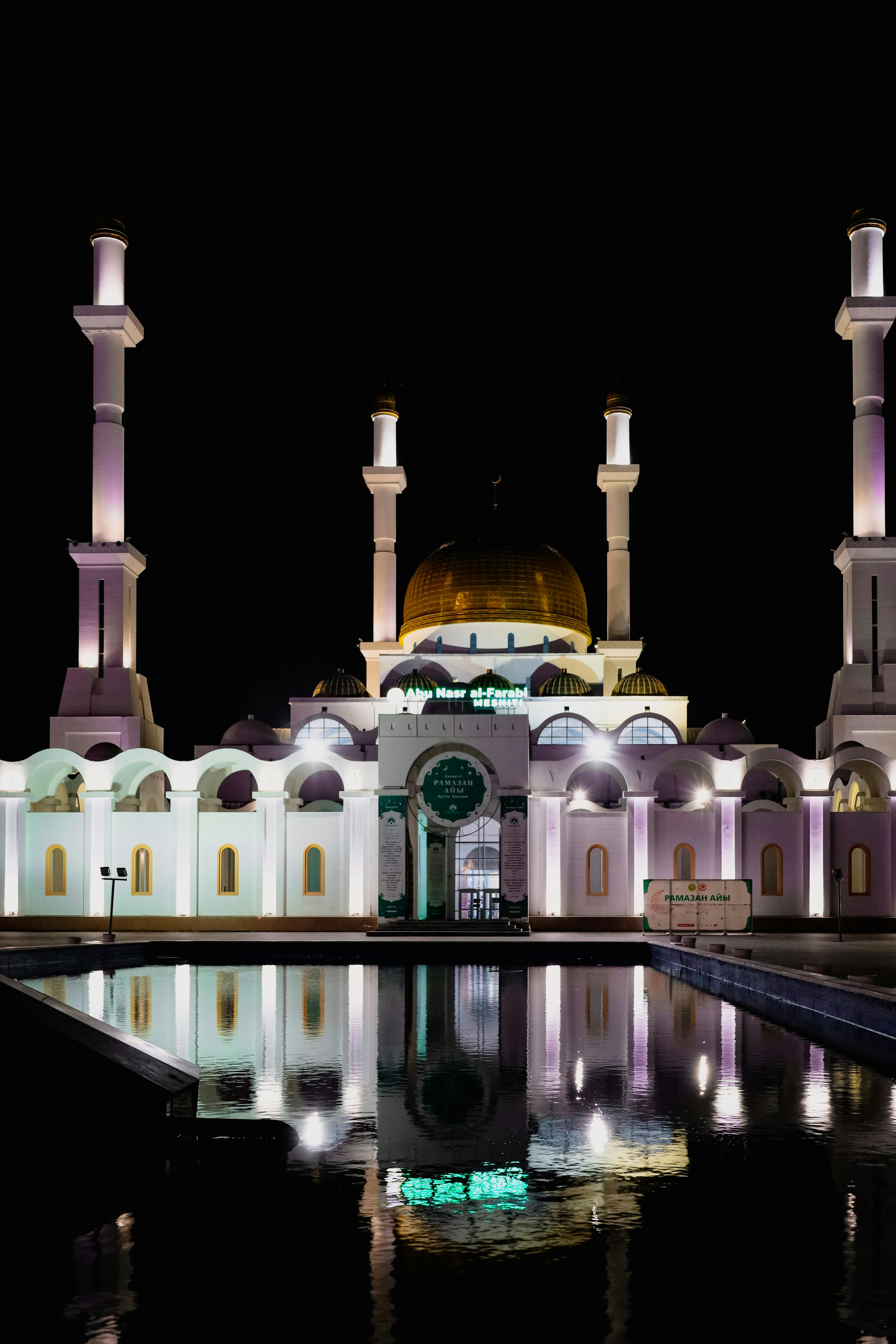 The stunning Nur-Astana Mosque reflecting in water, beautifully lit against the night sky.