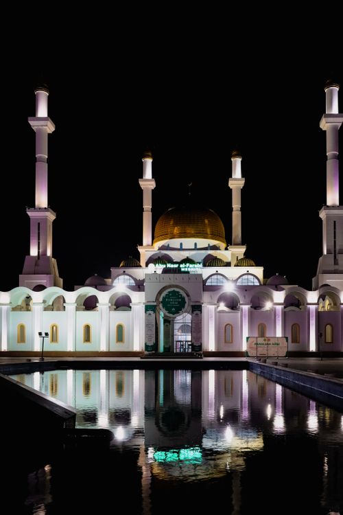 Free The stunning Nur-Astana Mosque reflecting in water, beautifully lit against the night sky. Stock Photo
