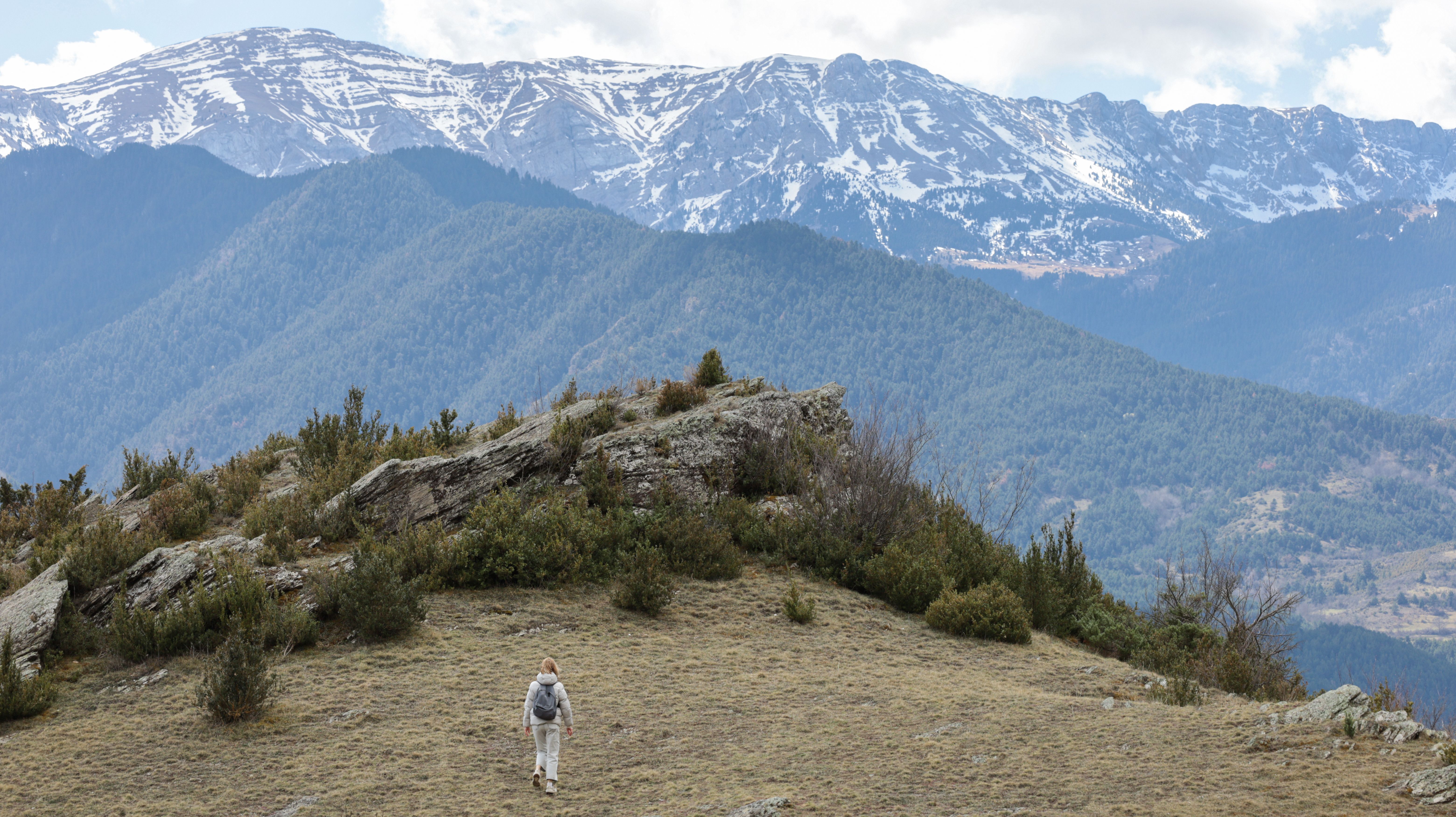 A lone hiker on a mountain slope with scenic snowcapped peaks in the background.