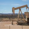 An active oil pumpjack operates in a dry, sunlit landscape under a clear blue sky.