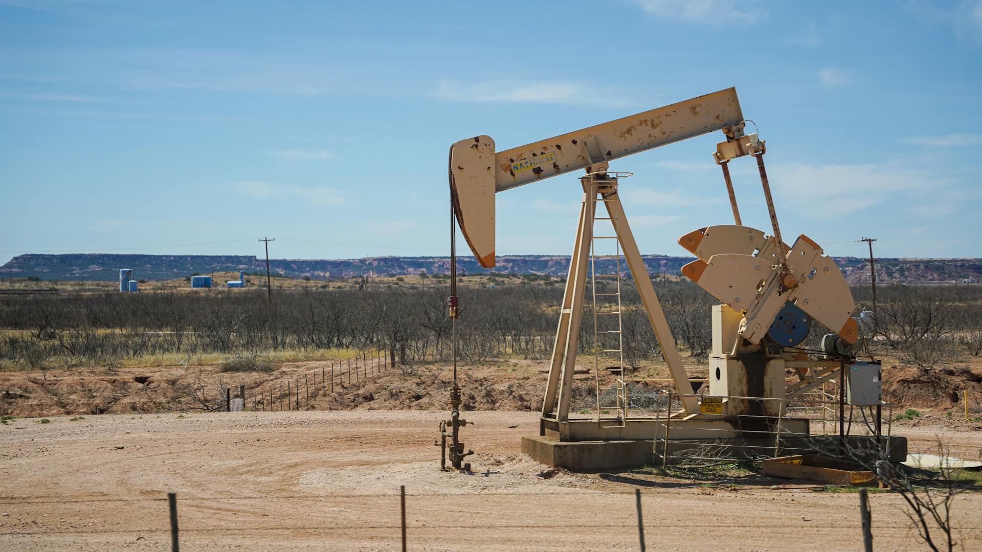 Industrial oil pumpjack in a desert setting under a clear blue sky, illustrating oil extraction technology.