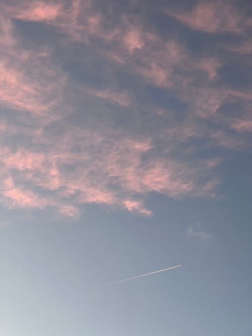 Free A serene evening sky featuring pink clouds and an airplane contrail at sunset. Stock Photo