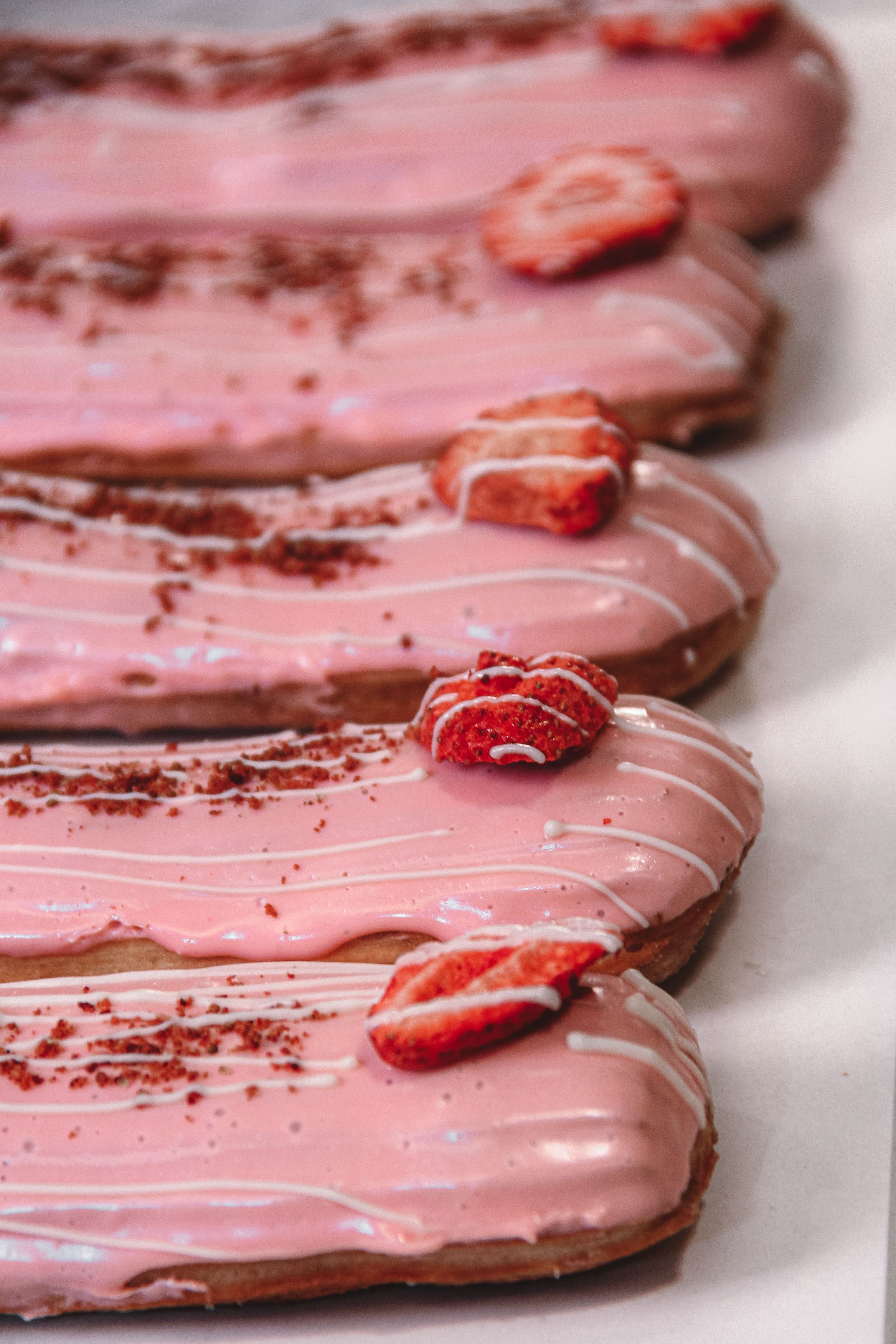 Close-up of strawberry-glazed eclairs adorned with sliced strawberries. Ideal for dessert inspiration.