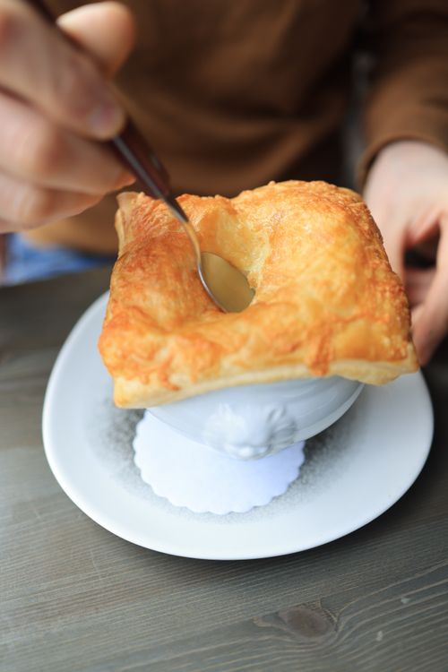 Free Close-up of a hand using a spoon to eat a soufflé topped with puff pastry. Stock Photo