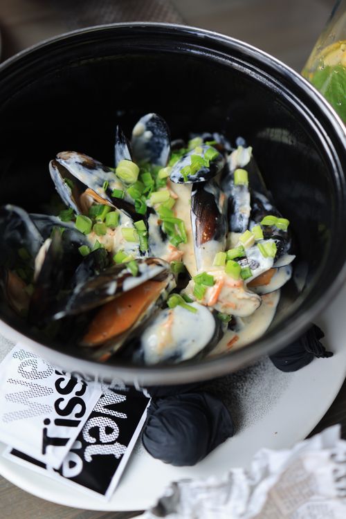 Free A black bowl of mussels topped with creamy sauce and fresh green onions. Stock Photo