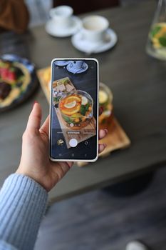 Close-up of smartphone photographing a citrus drink on a wooden table.