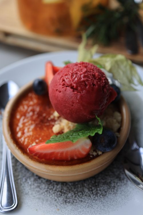 Free Close-up of a rich crème brûlée topped with a scoop of bold red sorbet and fresh berries. Stock Photo