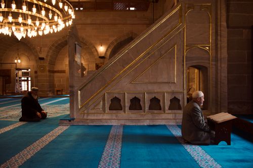 Free Two men engage in prayer inside a historic mosque, surrounded by intricate architecture and chandeliers. Stock Photo