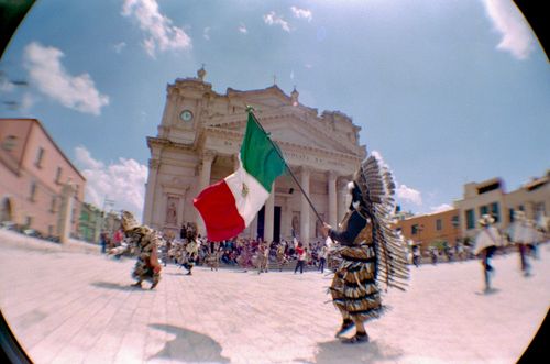 Free A colorful parade in Mexico with traditional costumes and a Mexican flag under a sunny sky. Stock Photo