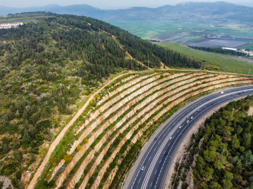 Free A breathtaking drone shot of a highway curving through a terraced hillside covered with lush forests and green fields. Stock Photo