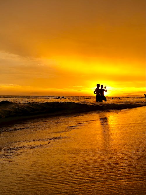 Free Men Silhouette on Sea Shore at Sunset Stock Photo