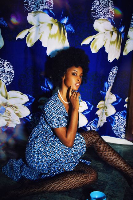 Stylish portrait of a woman in a blue dress with floral backdrop indoors.