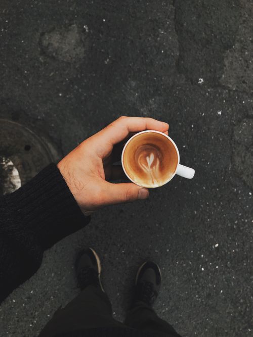 Free A top view of a hand holding a coffee cup with latte art on a pavement background. Stock Photo