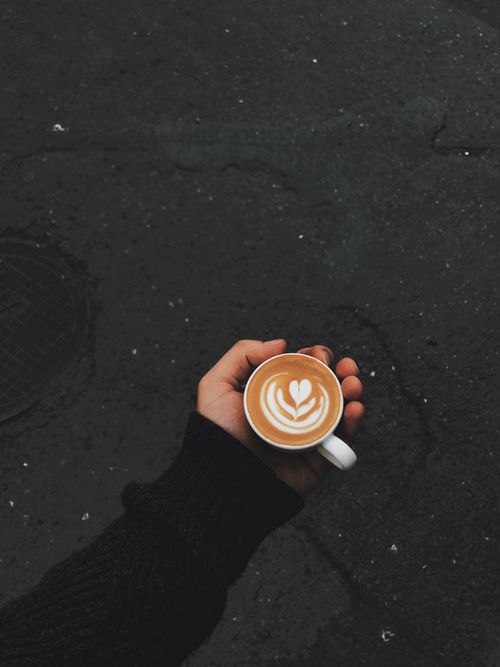 Free A hand holding a coffee cup with latte art in an outdoor setting, highlighting the coffee's design. Stock Photo
