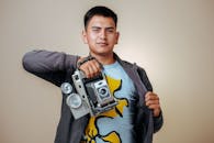Photo of a Young Man Holding a Vintage Camera on a Beige Background