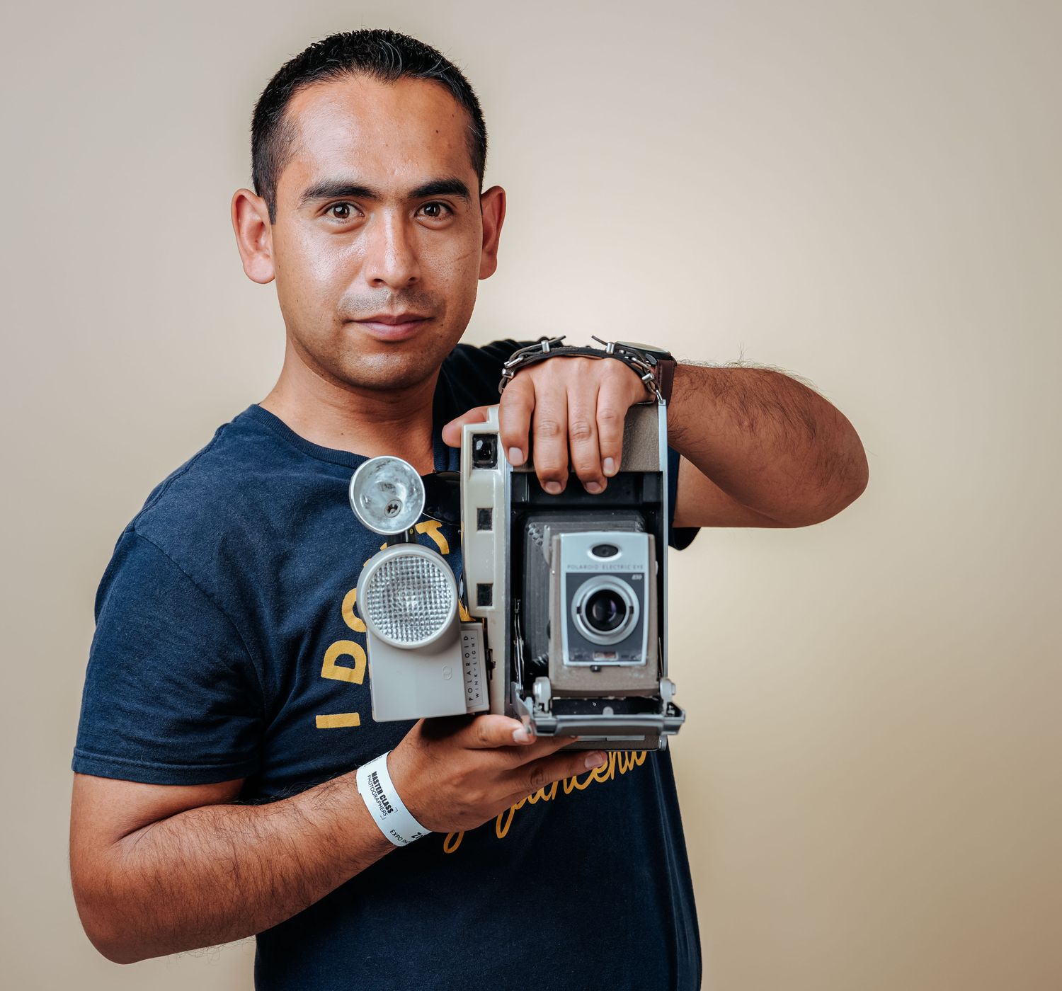 A man showcasing a retro camera in a studio setting with a beige background.