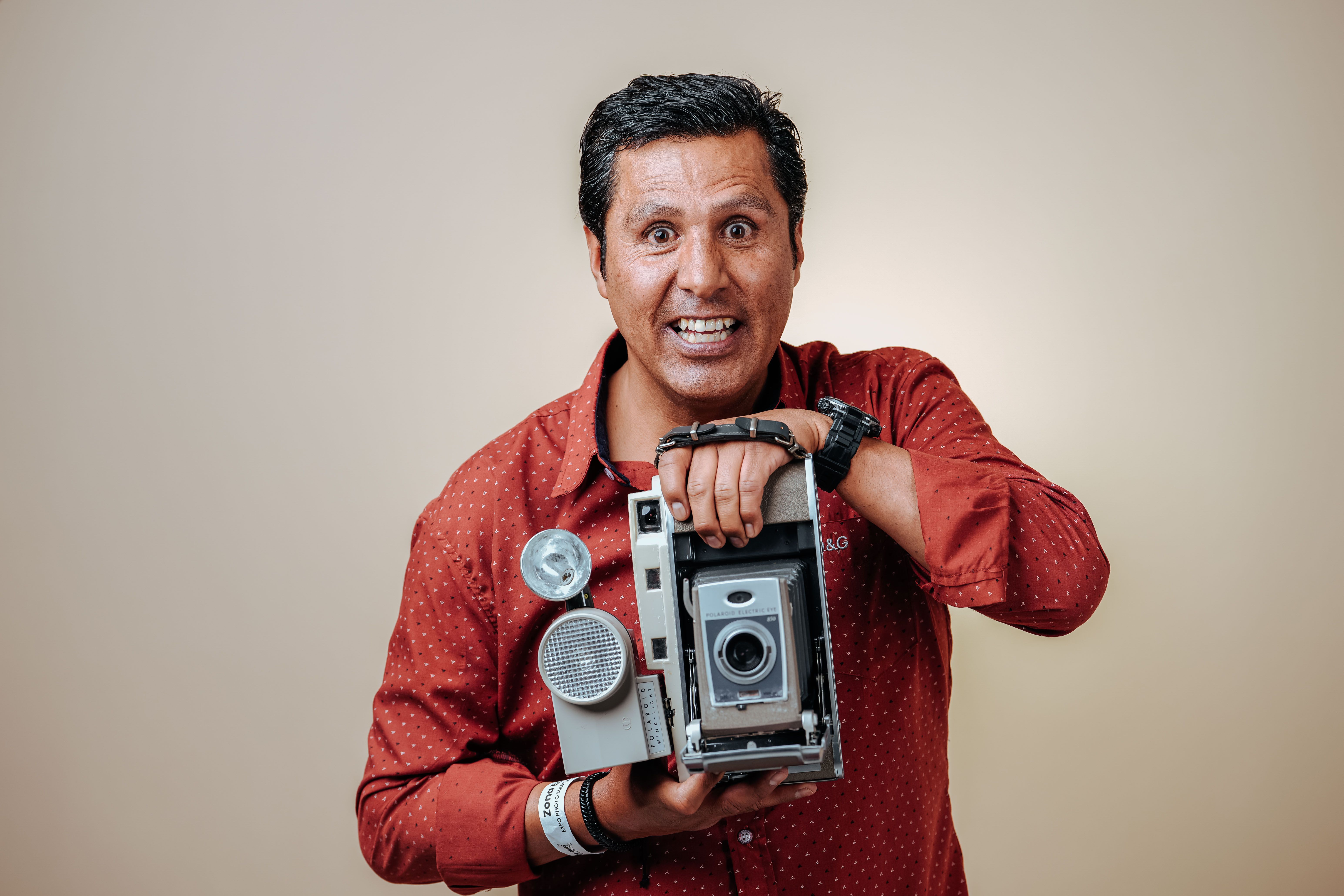 Happy man in a red shirt holds a vintage camera, showcasing a joyful moment in a studio setting.