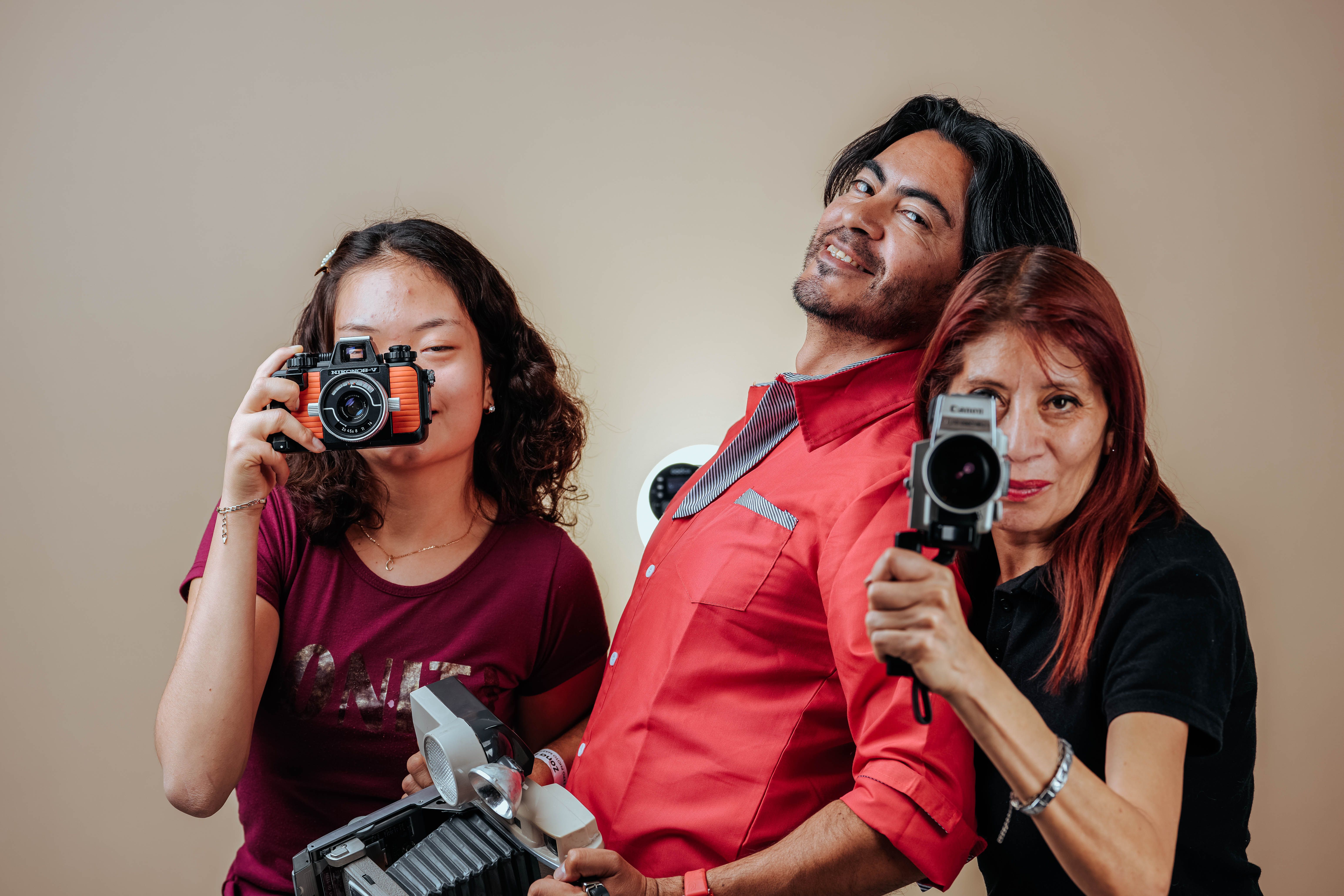 Three people posing with vintage cameras in a studio setting.