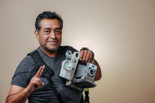 Free Smiling adult man posing with vintage camera in a studio setting. Stock Photo
