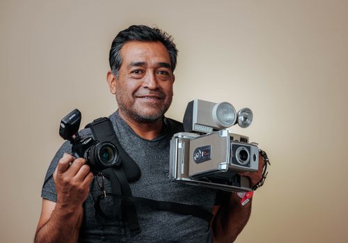 Free Smiling man holding vintage and modern cameras against a neutral background. Stock Photo