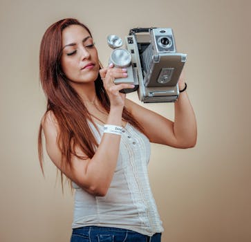 Young woman holding a retro camera in a studio setting, showcasing vintage photography style.
