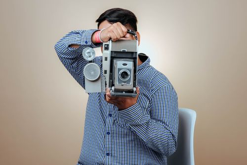 Free Portrait of a person holding a vintage camera, capturing retro vibes in a studio setting. Stock Photo