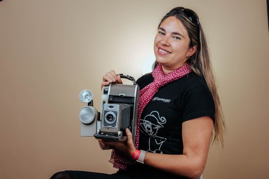 Woman smiling while holding a vintage camera in an indoor studio setting.