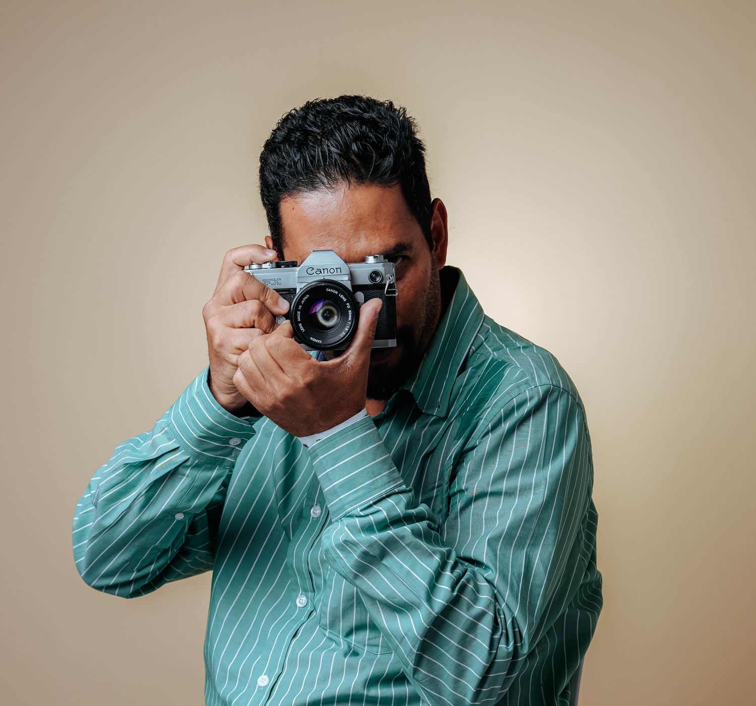 Man posing with a vintage camera in a studio setting wearing a striped green shirt.
