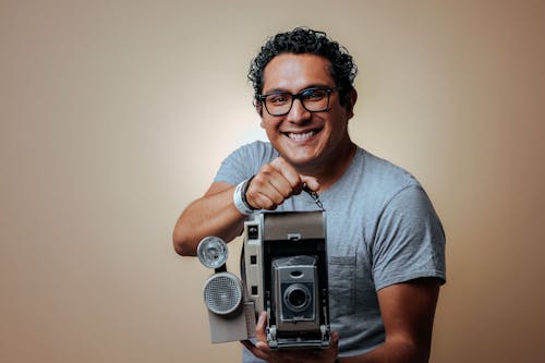 Smiling Man with Eyeglasses and Curly Hair Holding a Camera