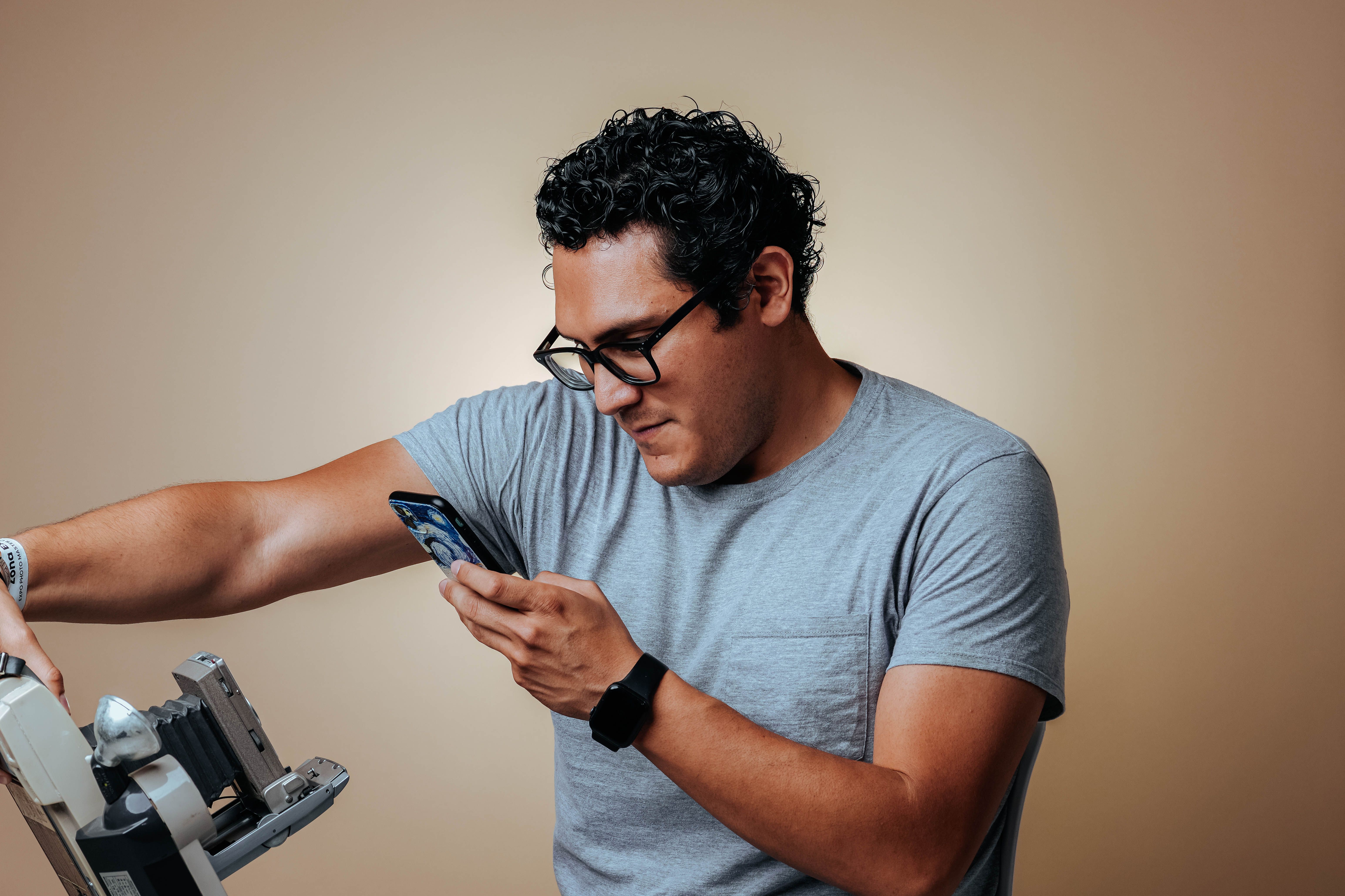 Man in gray shirt using a smartphone to photograph with studio equipment.