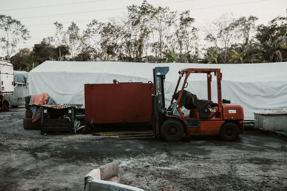 A red forklift parked in a rural area with equipment and trees in the background.