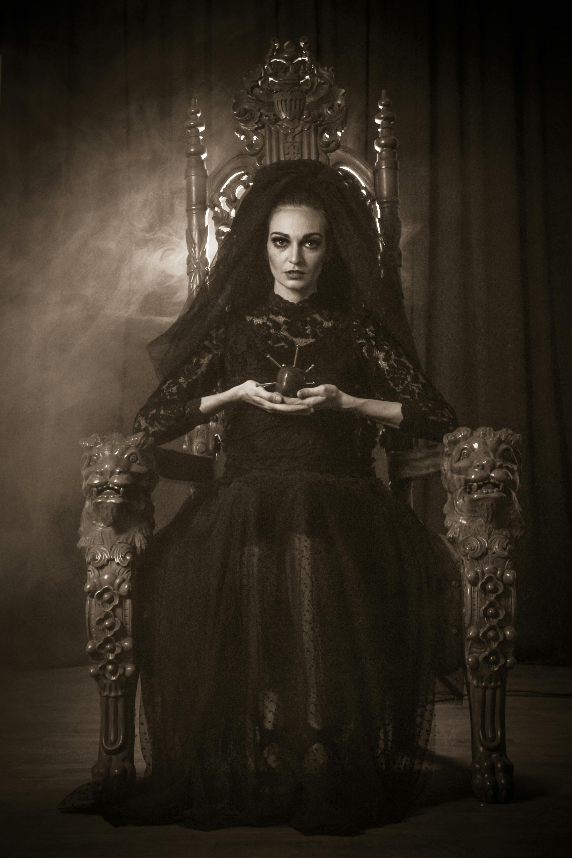 Dramatic gothic portrait of a woman in black and white seated on an elaborate throne.