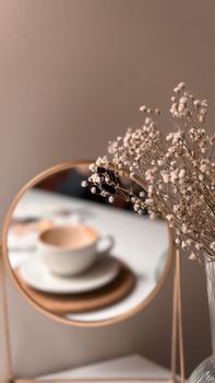 A cozy scene with a coffee cup reflected in a mirror alongside delicate flowers.