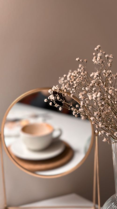 Free A cozy scene with a coffee cup reflected in a mirror alongside delicate flowers. Stock Photo