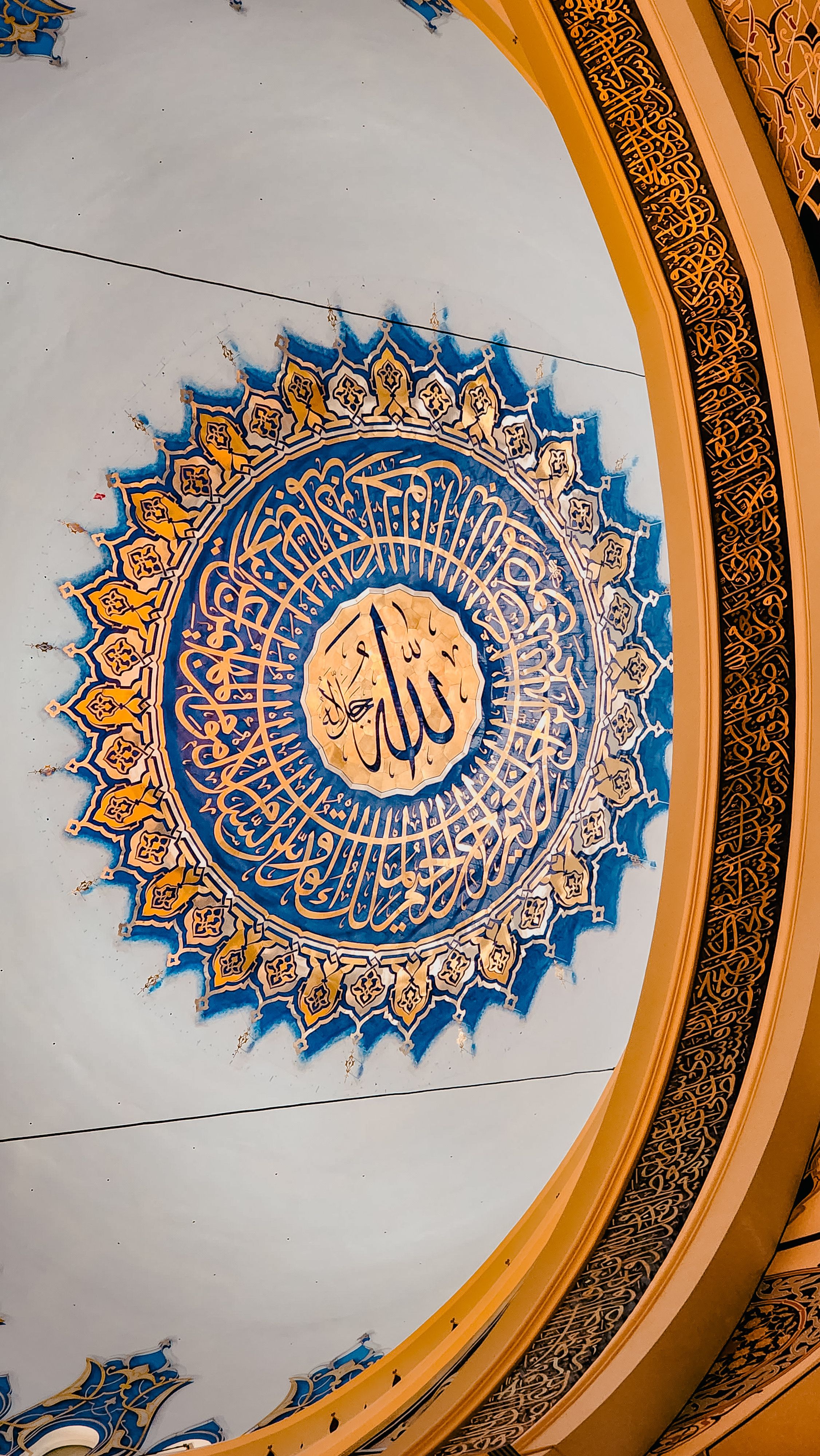 Close-up of detailed Islamic calligraphy art on a decorative ceiling, showcasing intricate Arabic patterns.
