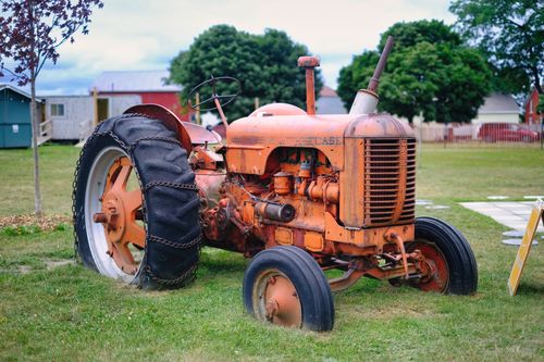 Free Classic orange tractor in a pastoral rural setting with greenery. Stock Photo