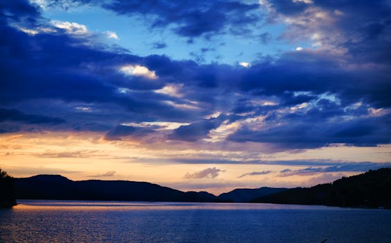 A stunning sunset over a calm lake, surrounded by serene mountains and dramatic clouds.