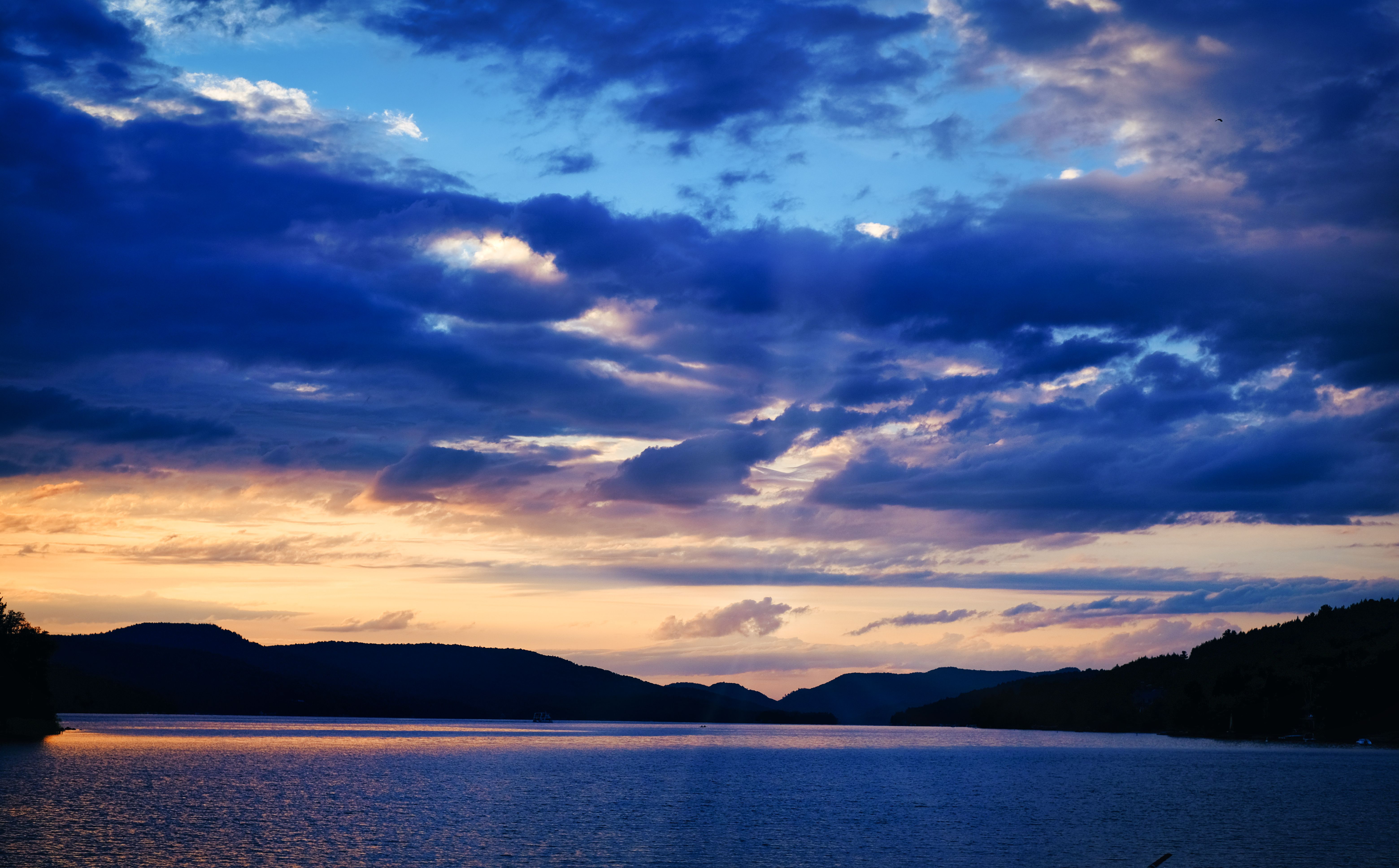 A sunset over a lake with clouds and mountains · Free Stock Photo
