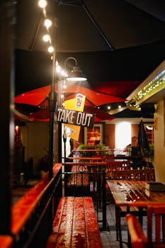 Romantic outdoor restaurant with takeout sign under string lights, creating a cozy ambiance.