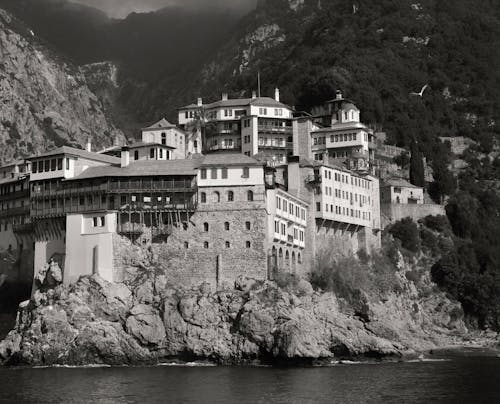 Landscape Photography of Gray and White House Near Mountain Cliffs Above Body of Water